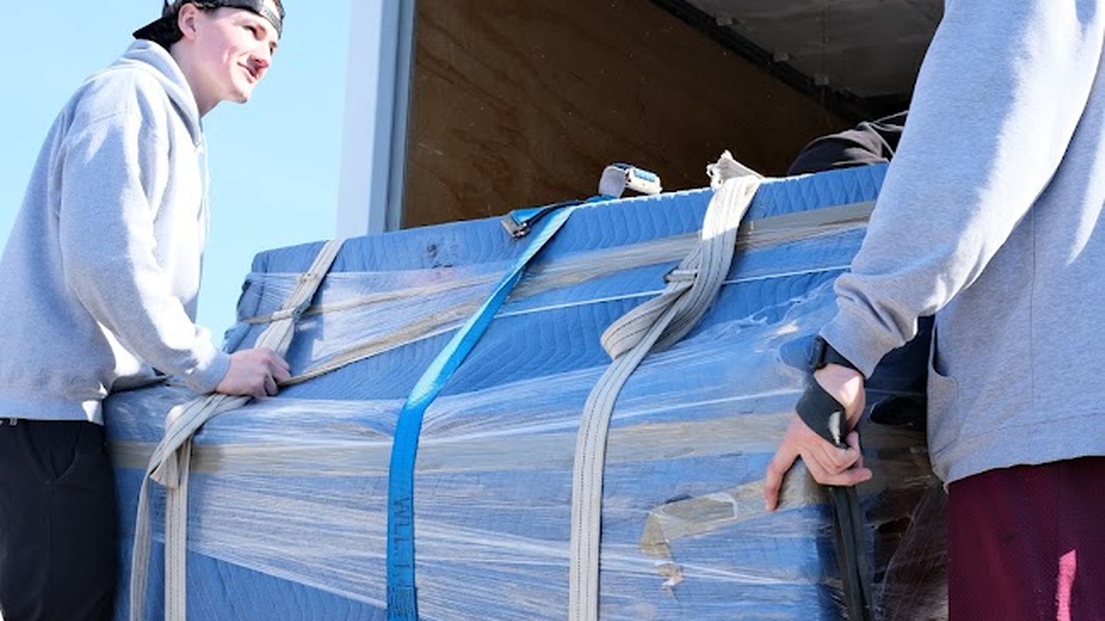 Two Big League Movers crew members carefully loading a wrapped piece of furniture into the truck